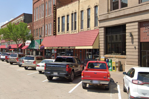 A street view of a downtown area with parked cars and a bakery with a coffee shop sign.