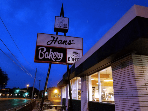 Sign for "Hans' Bakery" with a coffee symbol, illuminated at dusk, showcasing a cozy bakery exterior.