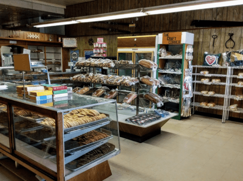 A cozy bakery interior with glass display cases filled with various baked goods and a shelf of packaged treats.