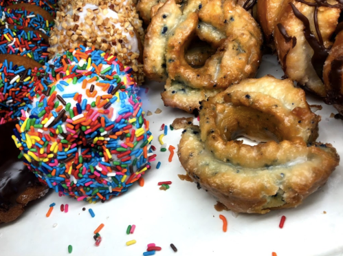 A colorful assortment of donuts, including a glazed donut with sprinkles and a twisted pastry, on a white plate.