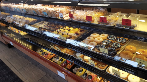 A display case filled with various pastries, donuts, and baked goods, neatly arranged with labels.