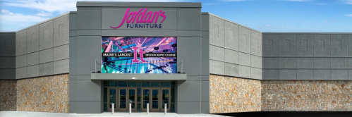 Exterior view of Jordan's Furniture store featuring a large digital sign and a stone-accented facade.