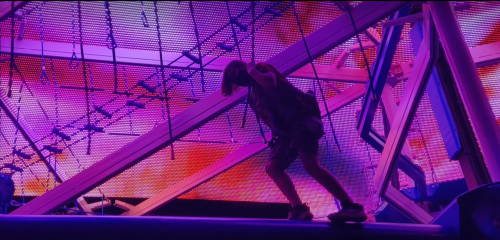 A person skateboarding under vibrant, colorful lights in a modern, geometric setting.