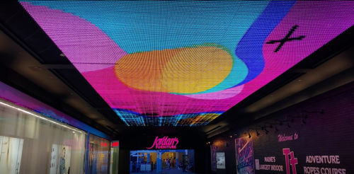 Colorful LED ceiling display with abstract patterns at Jordan's Furniture entrance, featuring vibrant pink and yellow hues.