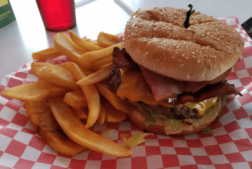 A sesame seed bun burger with cheese, bacon, and lettuce, served with a side of golden French fries.