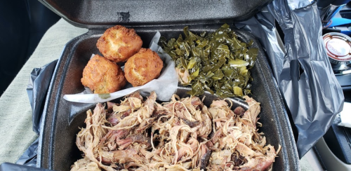 A takeout container with pulled pork, collard greens, and cornbread muffins.