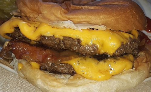 Close-up of a juicy cheeseburger with two beef patties, melted cheese, and crispy bacon on a toasted bun.