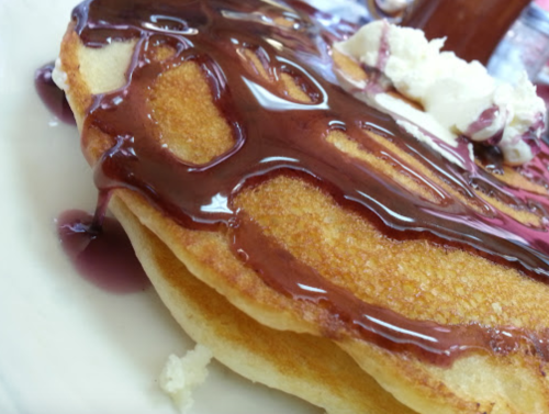 Close-up of fluffy pancakes drizzled with chocolate syrup and topped with a dollop of whipped cream.