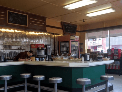 A retro diner interior with a counter, stools, and a worker preparing food in a cozy, nostalgic atmosphere.