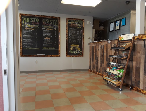 Interior of a pasta shop featuring chalkboard menus on the wall and a wooden display rack with snacks.