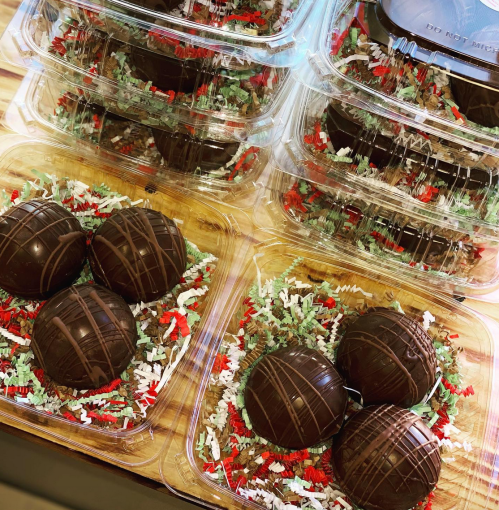 Chocolate truffles arranged in clear containers with festive red and green shredded paper.