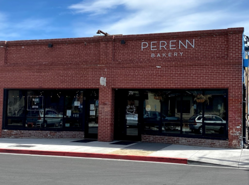 Exterior of Peren Bakery, a brick building with large windows and a sign, under a blue sky.