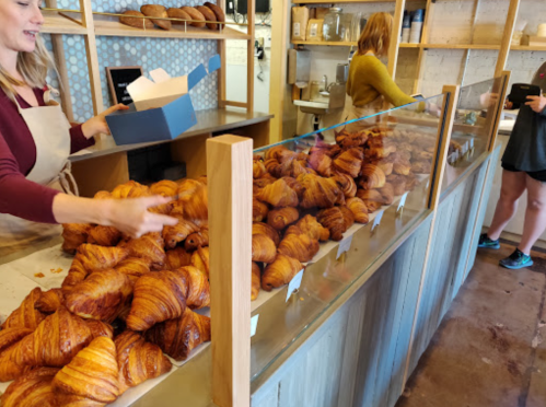 A bakery display filled with freshly baked croissants, with a staff member serving customers in the background.
