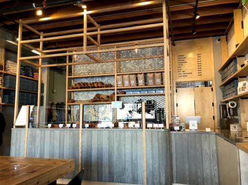 A modern café interior featuring a wooden counter, shelves with baked goods, and a menu on the wall.