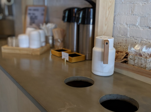 A coffee station with two large containers, a white pitcher, and various utensils on a countertop.