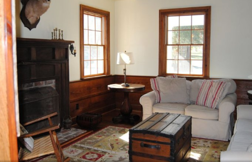 Cozy living room with a sofa, wooden coffee table, lamp, and windows, featuring rustic decor and warm lighting.