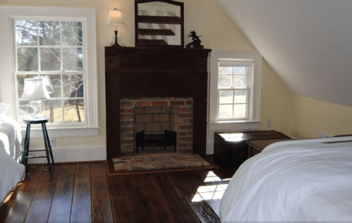Cozy bedroom with a fireplace, wooden floors, and large windows letting in natural light.
