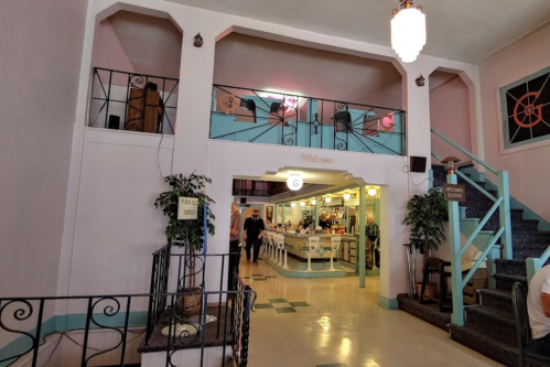 Interior of a vintage-style building with pastel colors, a welcome sign, and a staircase leading to an upper level.