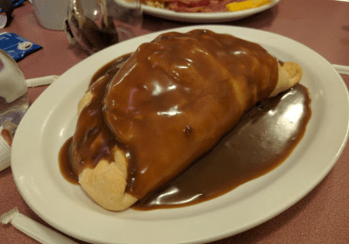 A large, golden-brown calzone topped with a thick, brown gravy on a white plate.