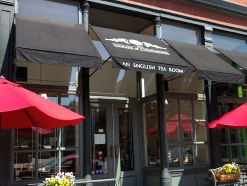Exterior of an English tea room with black awnings and red umbrellas at outdoor seating.