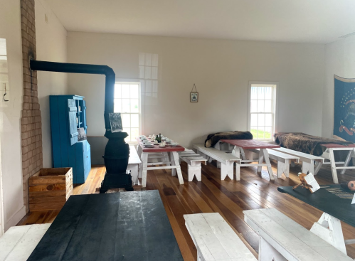 Interior of a simple room with wooden benches, a black stove, and a blue cabinet, featuring a rustic, cozy atmosphere.
