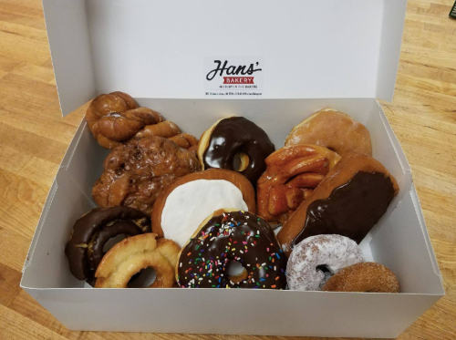 A box of assorted donuts, including glazed, chocolate-covered, and sprinkled varieties, on a wooden surface.