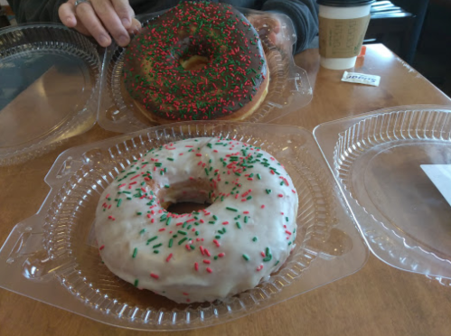 Two festive donuts on a table: one chocolate with green and red sprinkles, and one white icing with similar sprinkles.