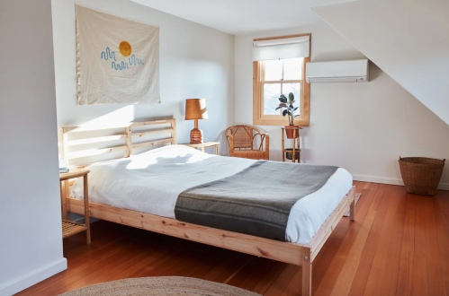 Bright, minimalist bedroom with a wooden bed, warm tones, and natural light from a window. Cozy decor elements included.