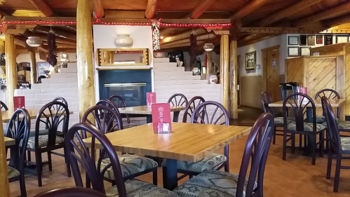 Cozy restaurant interior with wooden beams, tables, and a fireplace, decorated with warm lighting and rustic decor.