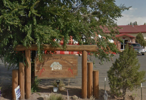 Sign for "Mountain View Resort" surrounded by trees, with a building and parking lot in the background.