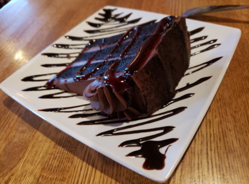 A slice of chocolate cake drizzled with chocolate sauce on a decorative plate.