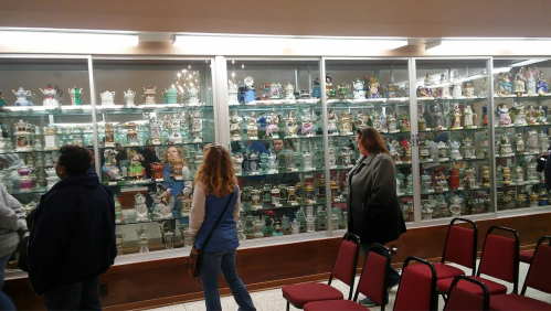 A display case filled with various figurines, with visitors observing the collection in a museum-like setting.