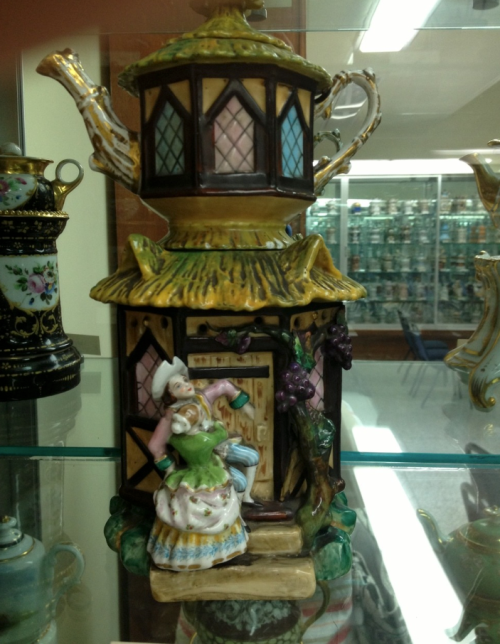 A decorative teapot shaped like a house, featuring a woman in traditional attire and colorful details.