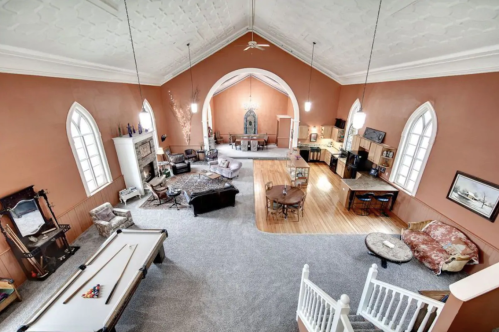 Spacious, elegantly designed interior with high ceilings, large windows, and a mix of seating areas and a pool table.
