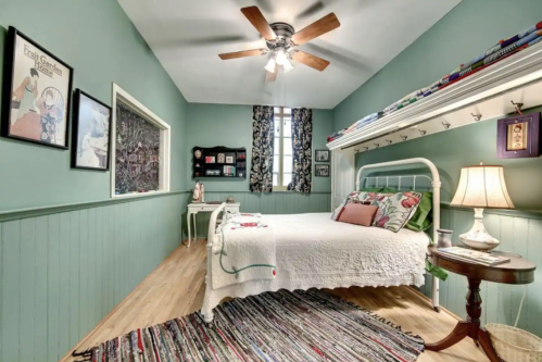 Cozy bedroom with a green accent wall, a bed with a quilt, a ceiling fan, and decorative artwork.