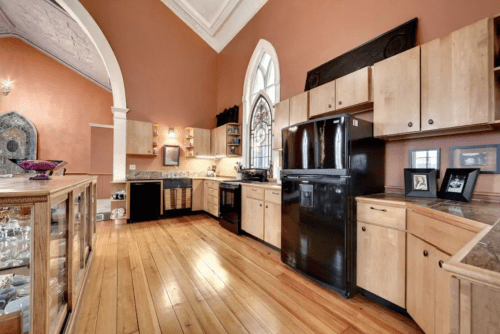 A spacious kitchen with wooden floors, modern appliances, and large windows featuring a stained glass design.