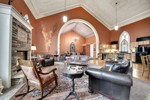 Cozy living space with high ceilings, warm orange walls, elegant furniture, and a decorative fireplace.