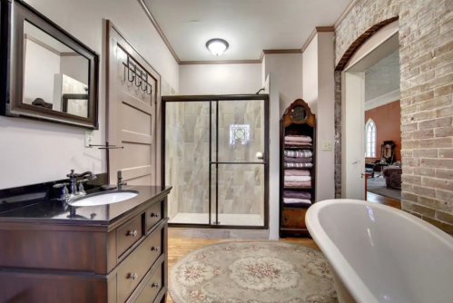 A modern bathroom featuring a glass shower, freestanding tub, dark wood vanity, and decorative rug.