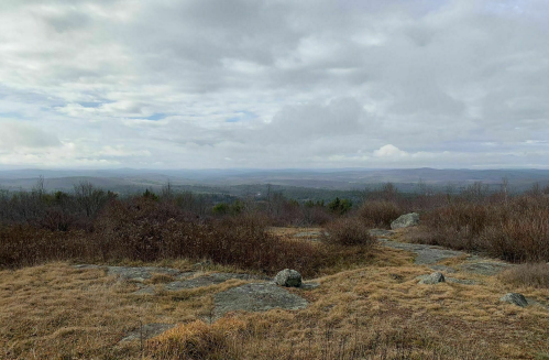 A scenic view of a vast landscape with rolling hills, rocky terrain, and a cloudy sky.