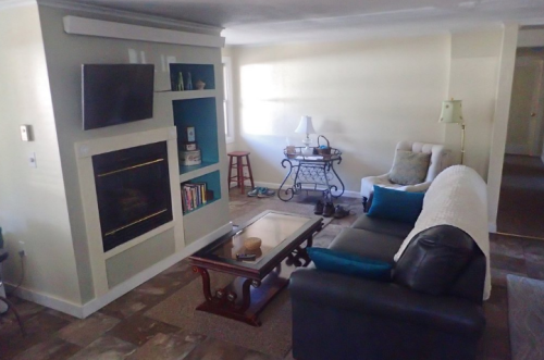 Cozy living room with a fireplace, TV, bookshelf, and comfortable seating, featuring light colors and a warm atmosphere.
