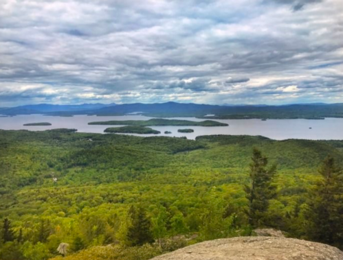 A panoramic view of a lush green landscape with a lake and islands under a cloudy sky.