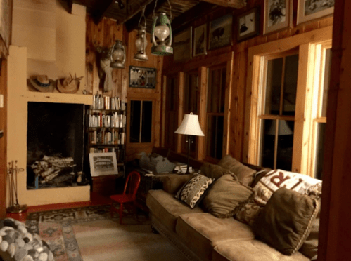 Cozy wooden living room with a fireplace, bookshelves, a sofa, and decorative lanterns on the walls.