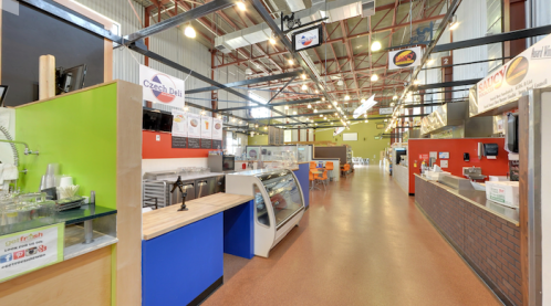Interior of a food hall featuring various vendor stalls, colorful decor, and seating areas. Bright and spacious atmosphere.