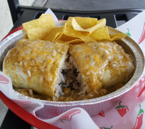 A plate of a burrito topped with sauce and cheese, served with tortilla chips on the side.