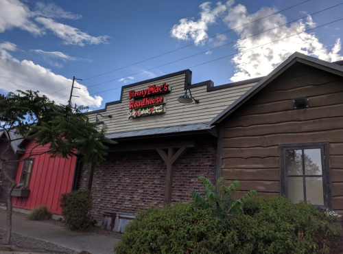 Exterior of Jimmy Mac's Roadhouse, featuring a wooden facade and a sign against a blue sky with clouds.