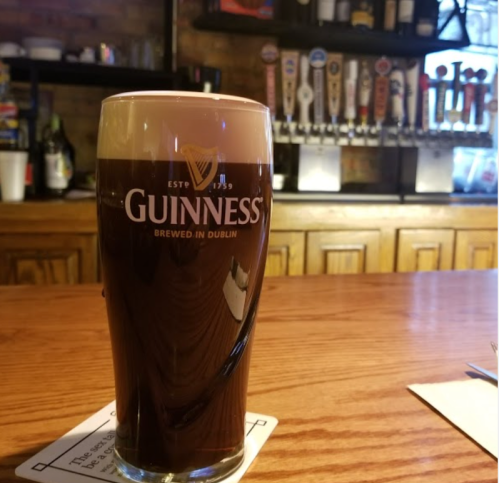 A pint of Guinness beer sits on a bar counter, with taps and bottles in the background.