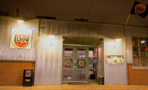 Exterior of a bar with a corrugated metal facade, featuring a sign that reads "Fiddler's Elbow" and illuminated entryway.