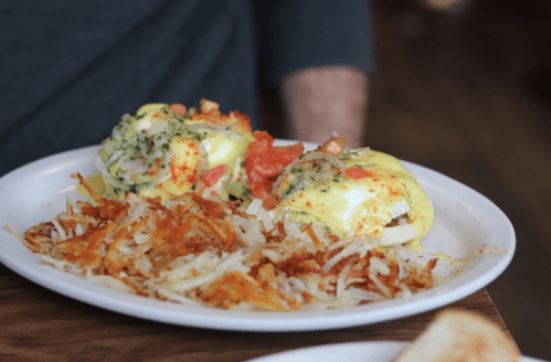 A plate of eggs Benedict topped with herbs and diced tomatoes, served with crispy hash browns on the side.