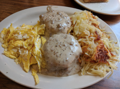 A plate of breakfast featuring scrambled eggs, biscuits with gravy, and crispy hash browns.