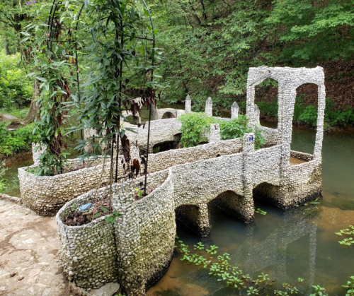 A whimsical stone bridge with arches over a serene pond, surrounded by lush greenery and trees.